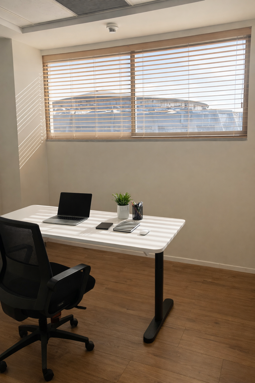 וילון ונציאני מעץ (או דמוי עץ) על חלון גבוה בחדר עבודה עם שולחן לבן מינימליסטי.