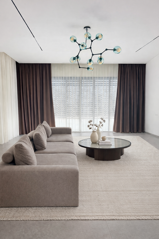 וילונות לסלון בשילוב צבעים של חום כהה ולבן עם גוף תאורה מעוצב וספה אפורה.