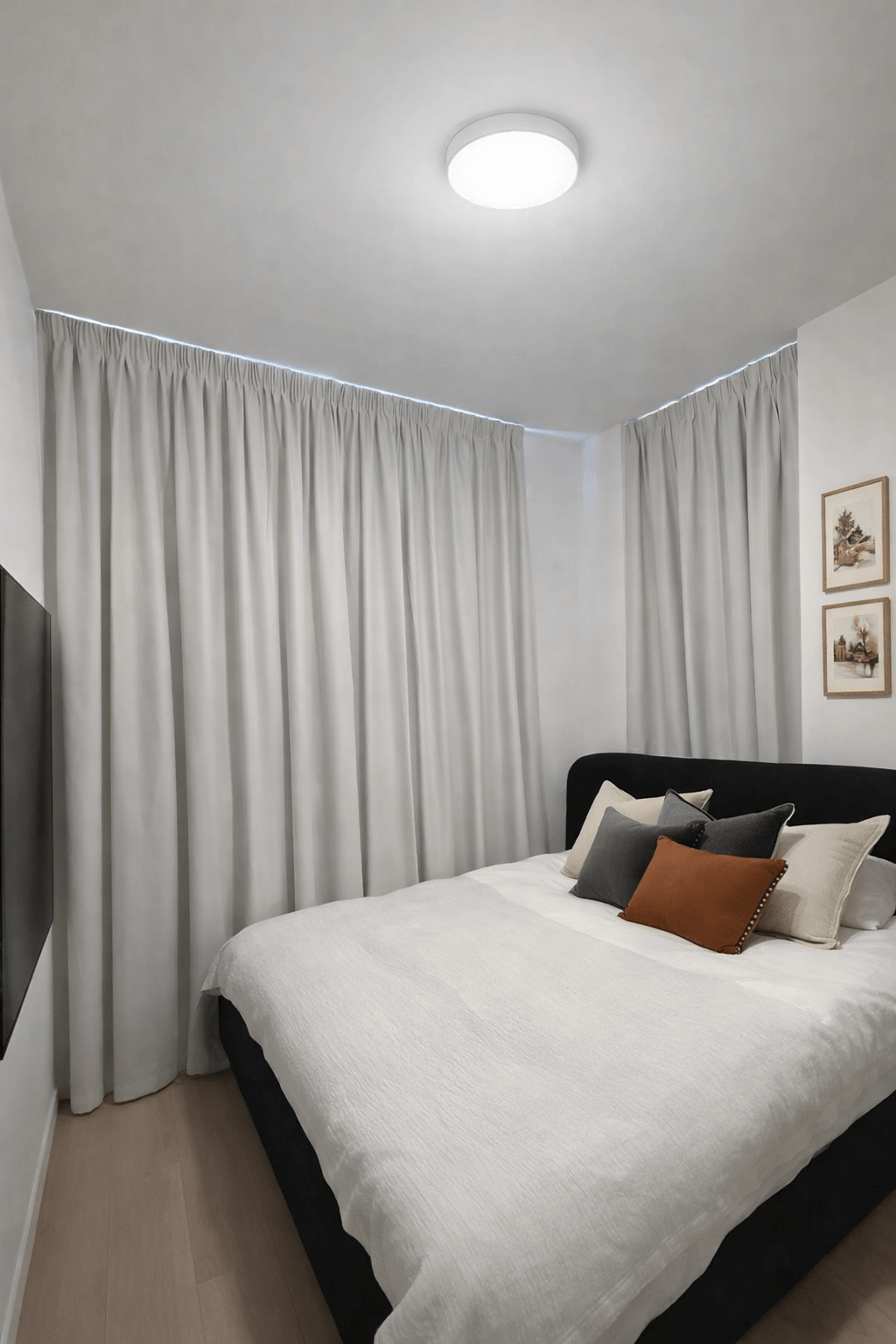 וילון בד אפור בהיר ארוך מהתקרה בחדר שינה מודרני עם מיטה שחורה וכרית כתומה.