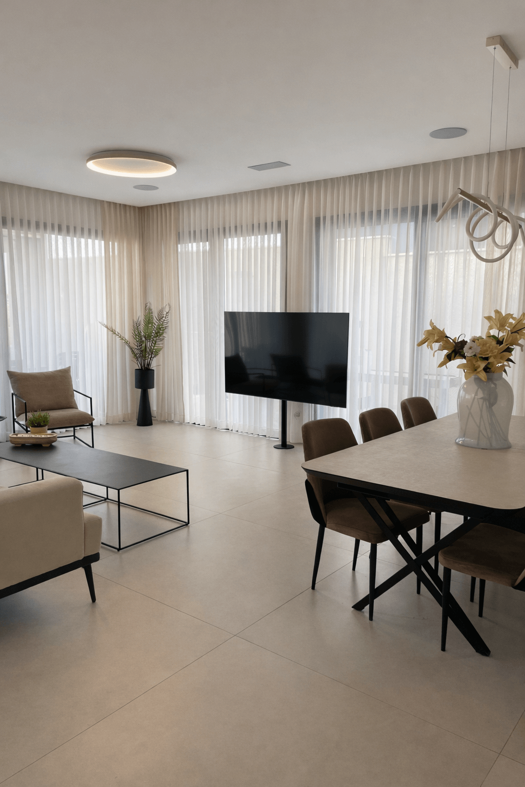 חלל מגורים פתוח הכולל פינת אוכל עם כיסאות חומים, שולחן אוכל מודרני ווילונות הצללה היקפיים.