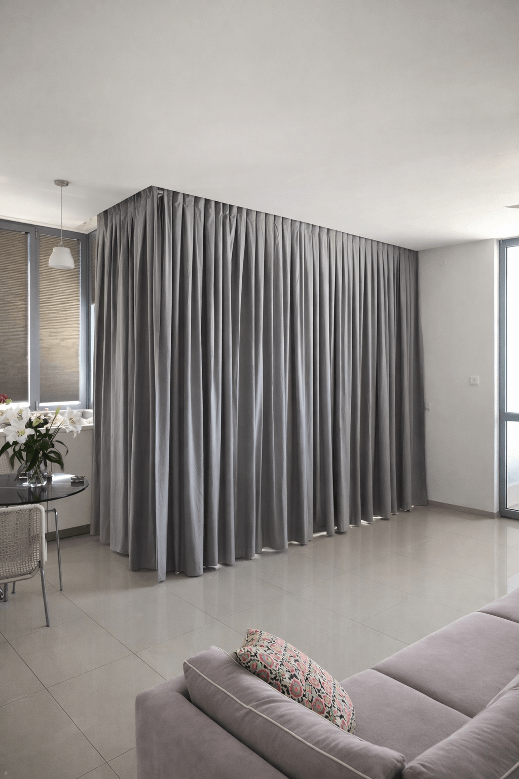 וילון הסטה אפור ארוך המשמש כחוצץ חלל בתוך דירה מעוצבת עם פינת אוכל וספה.