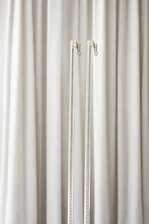 זוג מוטות משיכה שקופים (אקריליים) לוילונות הסטה על רקע וילון בד לבן.