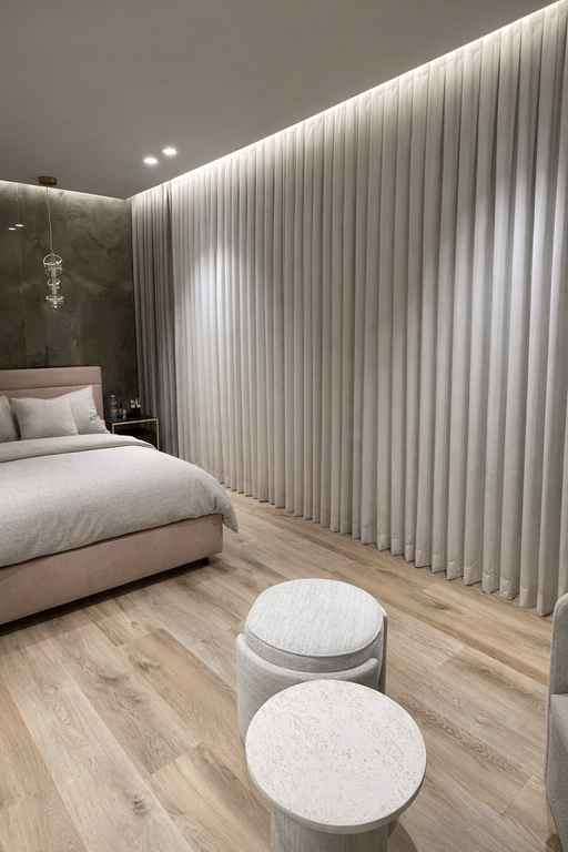 וילונות לחדר שינה מבד נופל בגוון בהיר עם תאורת נסתרת בתקרה ועיצוב מודרני.