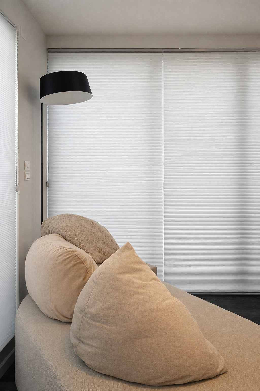 וילון גלילה לבן חלק המכסה חלון גדול מאחורי כורסת רביצה נוחה ופוף.