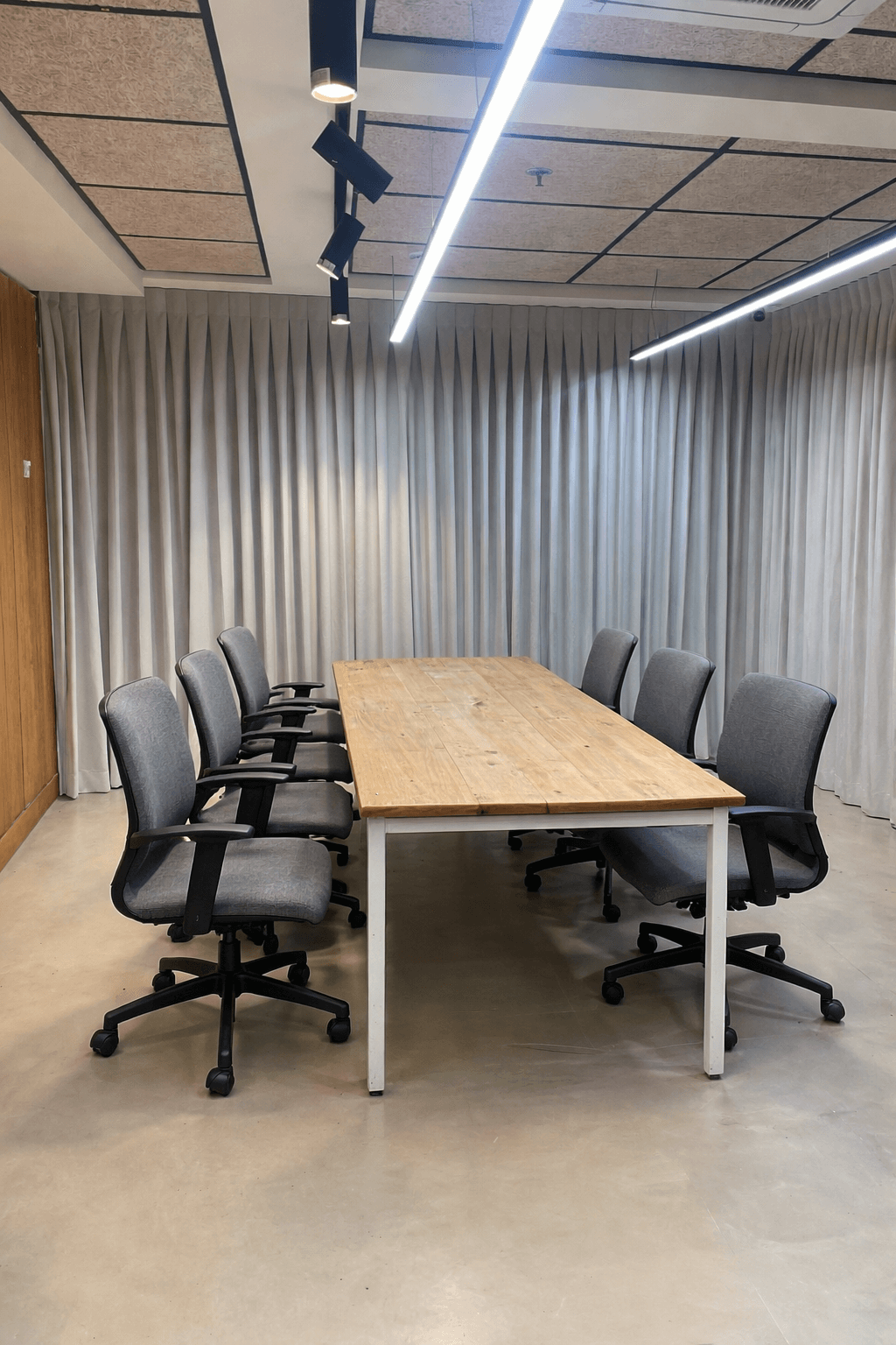 וילונות הסטה אפורים מקיר לקיר בחדר ישיבות עם שולחן עץ ארוך ותאורה משרדית.