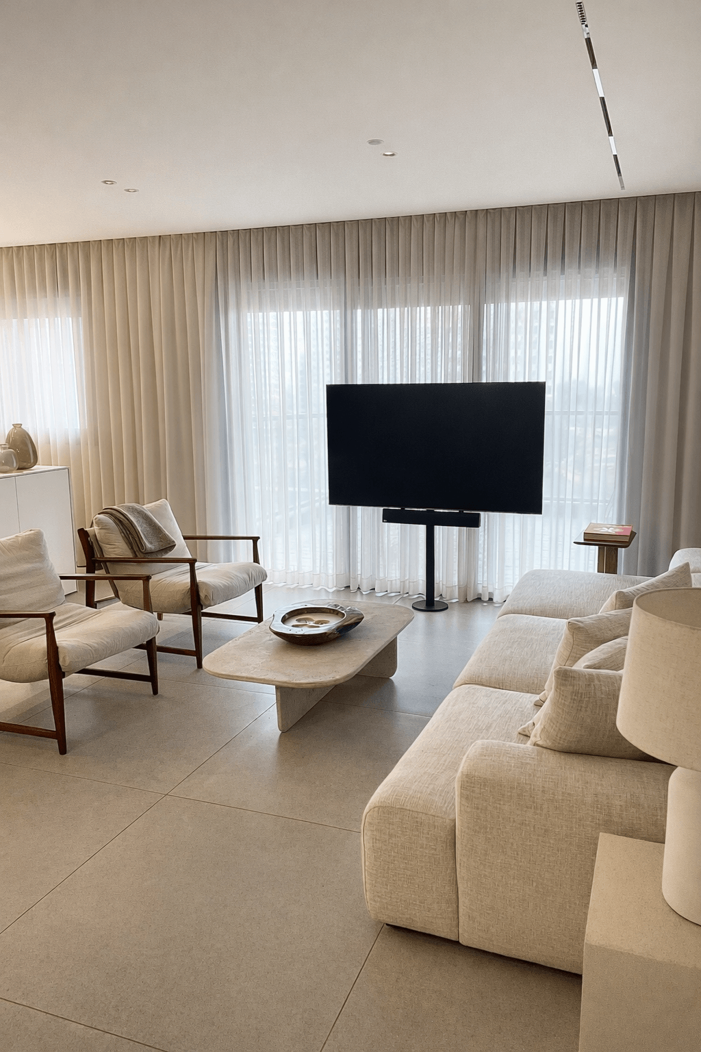 עיצוב סלון מודרני הכולל זוג כורסאות עם מסגרת עץ, שולחן קפה מאבן וטלוויזיה על עמוד.